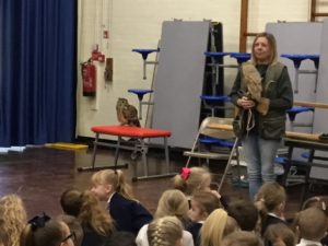 Photo of a visitor to the academy holding an Owl in her hands and delivering a presentation to a large group of pupils gathered in the main hall.