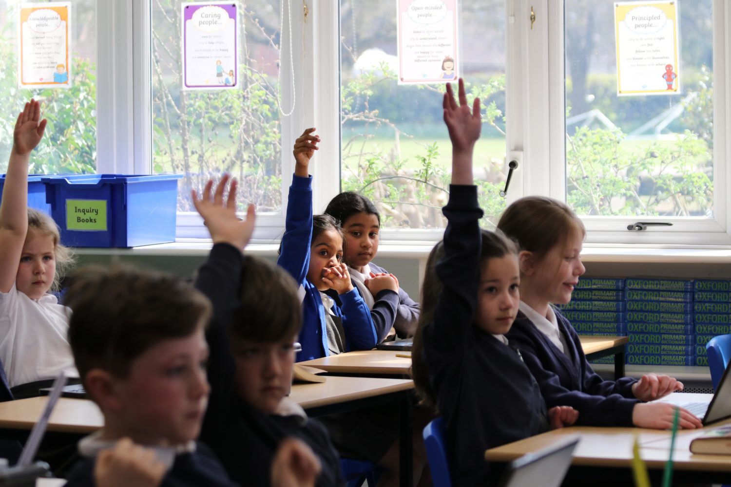 Multiple students with their hands up, waiting to answer a question in class.
