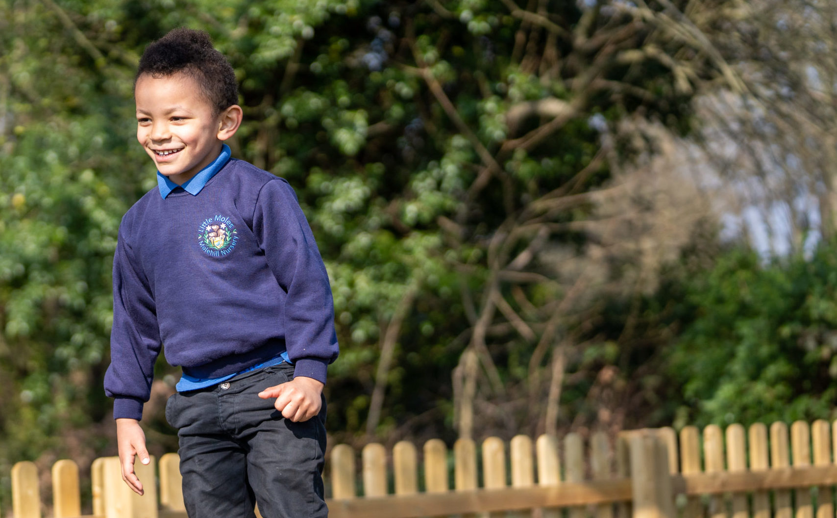 A young boy in Molehill Primary Academy uniform is seen smiling, whilst standing in a sunny outdoor area.